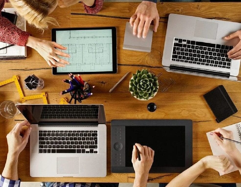A group of people sitting around a table with laptops.