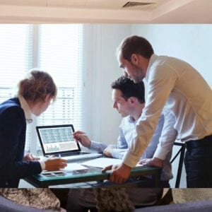 Three people are gathered around a laptop.