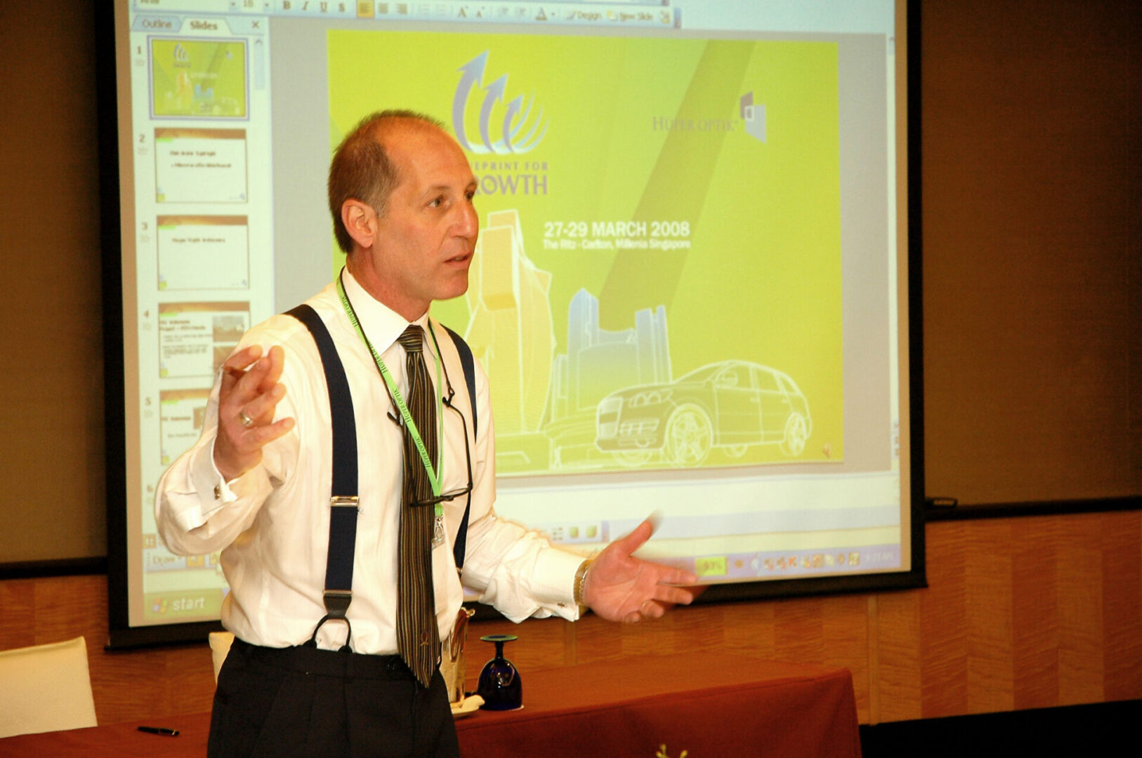 A man in suspenders standing next to a projector screen.